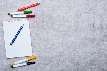  View of a notepad in a ticker, colored markers and a stylish blue pen on a gray background. Contains space for your lettering or insertion. The concept of business and creativity.