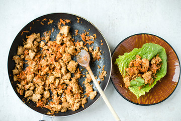 Top view of frying pan with cooked/sauteed ground turkey with shredded carrots and sweet soy sauce and lettuce cups finger food on a brown pottery plate. Overhead, close up. 