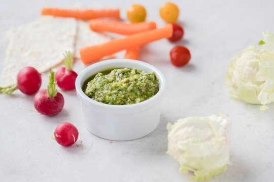 Mini vegetables served with pestos: avocado, hemp and pumpkin seeds pesto; almond, mint and basil pesto: walnut, kale and parsley pesto served with a silver spoon on light background. 