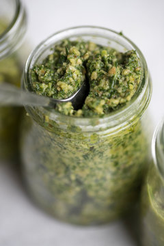 Three pestos in glass jars: avocado, hemp seeds and pumpkin seeds pesto; almond, mint and basil pesto: walnut, kale and parsley pesto served with a silver spoon on light background. 