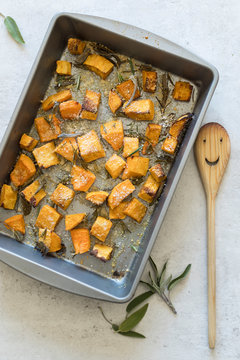 Top view of baking sheet/frying pan with oven baked butternut squash/pumpkin with sage leaves and shredded parmesan cheese and a wooden happy spoon. Flat lay, overhead, up high. . 