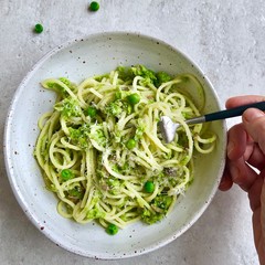Top view of hand holding a fork with vegan English baby sweet peas summer pasta with nutritional yeast. Overhead, close up, square picture. 