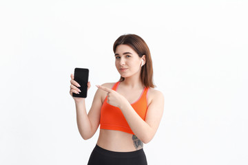 Young fitness woman posing isolated on a white background listening to music with wireless headphones.