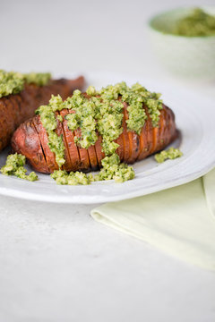 Hasselback baked sweet potatoes served with green walnut, kale and parsley pesto on white plate. Vertical, close up, copy space. 