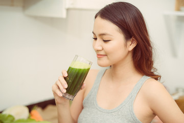 Pretty young woman drinking a vegetable smoothie in her kitchen