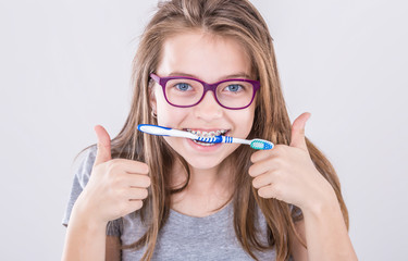 Girl from the dental braces with teethbrush making thumb up hand sign gesture. Orthodontist and dentist concept