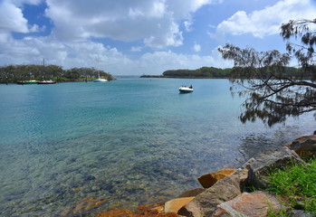 Boat on Mooloolah River on a sunny but cloudy day. Rock wall along Mooloolah river (Sunshine Coast, Queensland, Australia). Moored yachts in the marina.