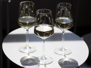 Three glasses with white dry wine on a table in a cafe lit by the bright sun