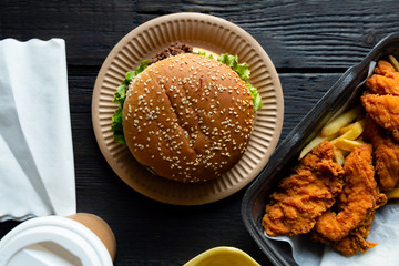 Hamburger, french fries and fried chicken in takeaway containers on the wooden background. Food...