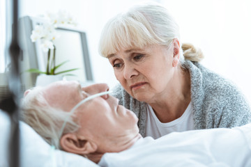 Obraz na płótnie Canvas sad senior woman looking at husband in coma in clinic