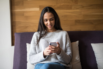 Pretty young girl using her smartphone on couch at home in the living room