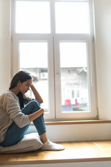 Sad depressed young woman having social problems sitting on windowsill