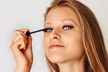 Fototapeta premium Beautiful woman holds brush of mascara and puts on cosmetics on her face. Make-up, cosmetics, beauty, eye lash extension