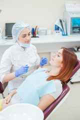 Young beautiful female dentist helps patient with toothache. A red-haired woman sits in a chair at the doctor and complains about the pain of caries. Dental services. Unhappy girl with pulpitis
