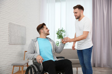 Volunteer giving glass of water to man in wheelchair at home. Helping disabled
