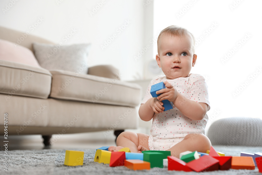 Wall mural Cute baby girl playing with building blocks in room. Space for text