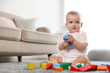 Cute baby girl playing with building blocks in room. Space for text