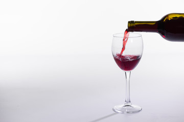 Red wine pouring into glass from bottle on white background with copy space