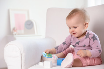 Cute baby girl playing with building blocks in armchair at home. Space for text