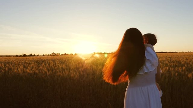 Mom and baby summer walks in field. travel mother and child. concept of happy family. A young mother with her little daughter is dancing and laughing in a wheat field, in rays of beautiful sunset.