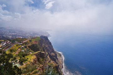 Top view from Cabo Girão Skywalk in Madeira island with blue ocean, clouds and city in background