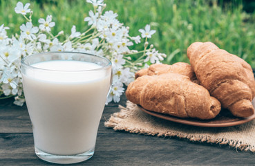 Next to the croissants and white flowers is a glass cup of milk.