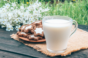 Next to the cookie and white flowers is a glass cup of milk on a napkin.