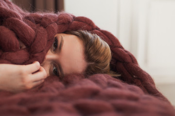 cute young blonde is lying on the bed wrapped in a brown cozy blanket. Warmth and comfort of home