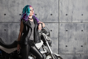 Fototapeta na wymiar Cool girl in leather clothes near the motorcycle. Young stylish woman with colored hair on the bike.