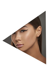 Cropped side geometric portrait of woman with black flicks. The girl with dark hair is wearing golden stud earrings in the shape of triangular pyramid, looking at camera behind triangle foreground.