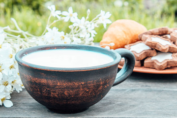 Next to the cookies and white flowers is a cup of milk on a wooden table.