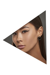 Cropped side geometric portrait of Korean lady with black flicks. The girl with dark hair is wearing black stud earrings in the shape of flat ring, looking at the camera behind triangle foreground.