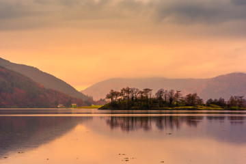 Loch leven at sunset, with mountains in the background and an island of trees reflected in the water. Glencoe, Scotland.