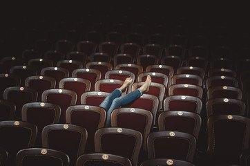 legs of a girl in jeans are shown from behind the seats in the theater