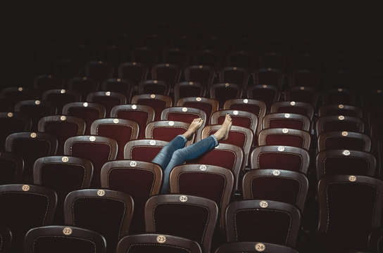 Legs Of A Girl In Jeans Are Shown From Behind The Seats In The Theater