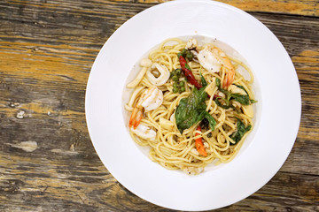 Top view seafood stir fried spicy spaghetti in white ceramic plate on wooden table in the restaurant.