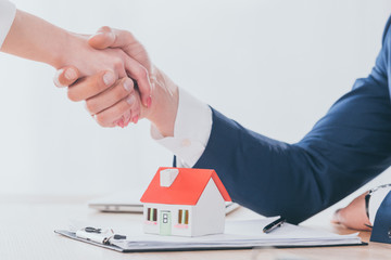 Fototapeta na wymiar partial view of realtor shaking hands with customer near house model on tabletop