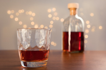 Whiskey in glass and big bottle on a wooden table. with bokeh on background