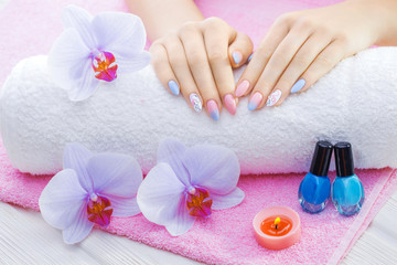 Obraz na płótnie Canvas beautiful colored manicure with decor, orchid, towel and candle on the white wooden table. spa
