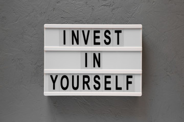 Lightbox with 'Invest in yourself' words on a gray background, top view. Overhead, flat lay, from above. Close-up.