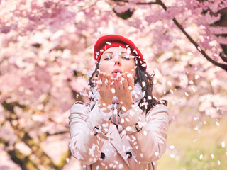 Beautiful Woman blowing petals in her hands, enjoying a flowering spring garden