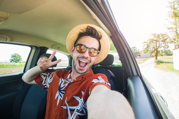 Happy young driver taking a selfie inside a car at vacation