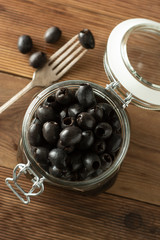 Black olives, pickled olives in jar on wooden background