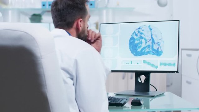 Doctor looking at 3D brain scan on the monitor of his computer in modern office or research center