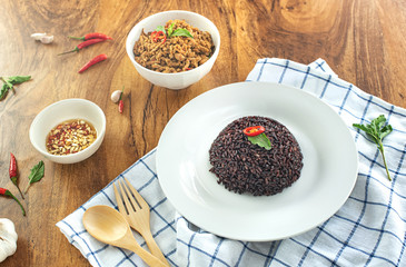 Rice berry in a plate and stir-fried minced pork basil in a bowl on a wooden table.