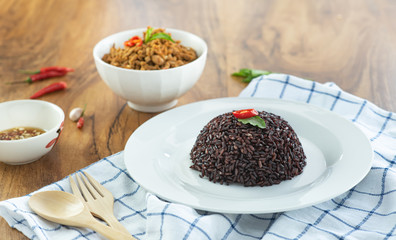 Rice berry in a plate and stir-fried minced pork basil in a bowl on a wooden table.