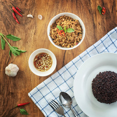 Stir fried basil with minced pork in a bowl and rice berries on the plate. put on a wooden table, top view