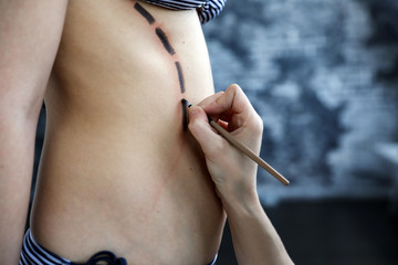 makeup artist draws lines on the body of a girl
