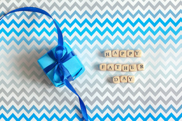 Happy Father's day greeting card with decorated blue gift box on zigzag striped background. Top...