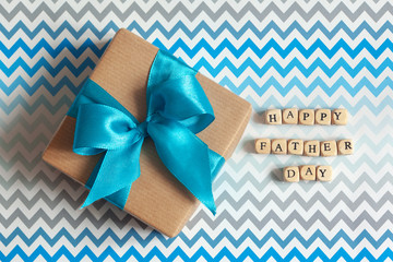 Happy Father's day greeting card with decorated gift box on zigzag striped background. Top view.